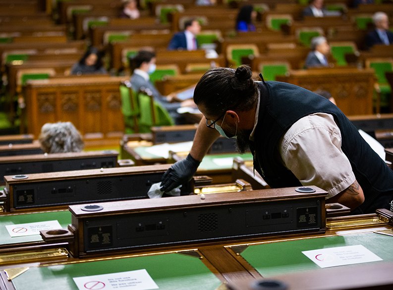 Photo of an employee cleaning a Member’s desk in the House of Commons Chamber
