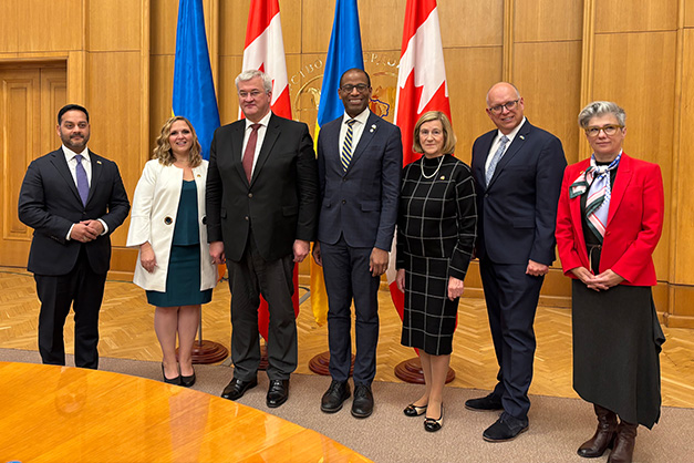 A delegation of members of the House of Commons visiting Ukraine, led by Speaker Fergus, pose in front of the Canadian and Ukrainian flags.