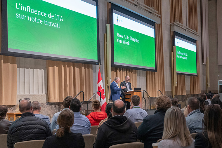 Two speakers present a slide on “AI's influence on our work” to an audience.